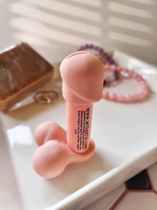 Penis shaped lip balm with removal head and balls. Neutral color penis shaped lip balm by Willy Stik. Penis shaped lip balm sitting on white plate. Created with organic soybean oil.